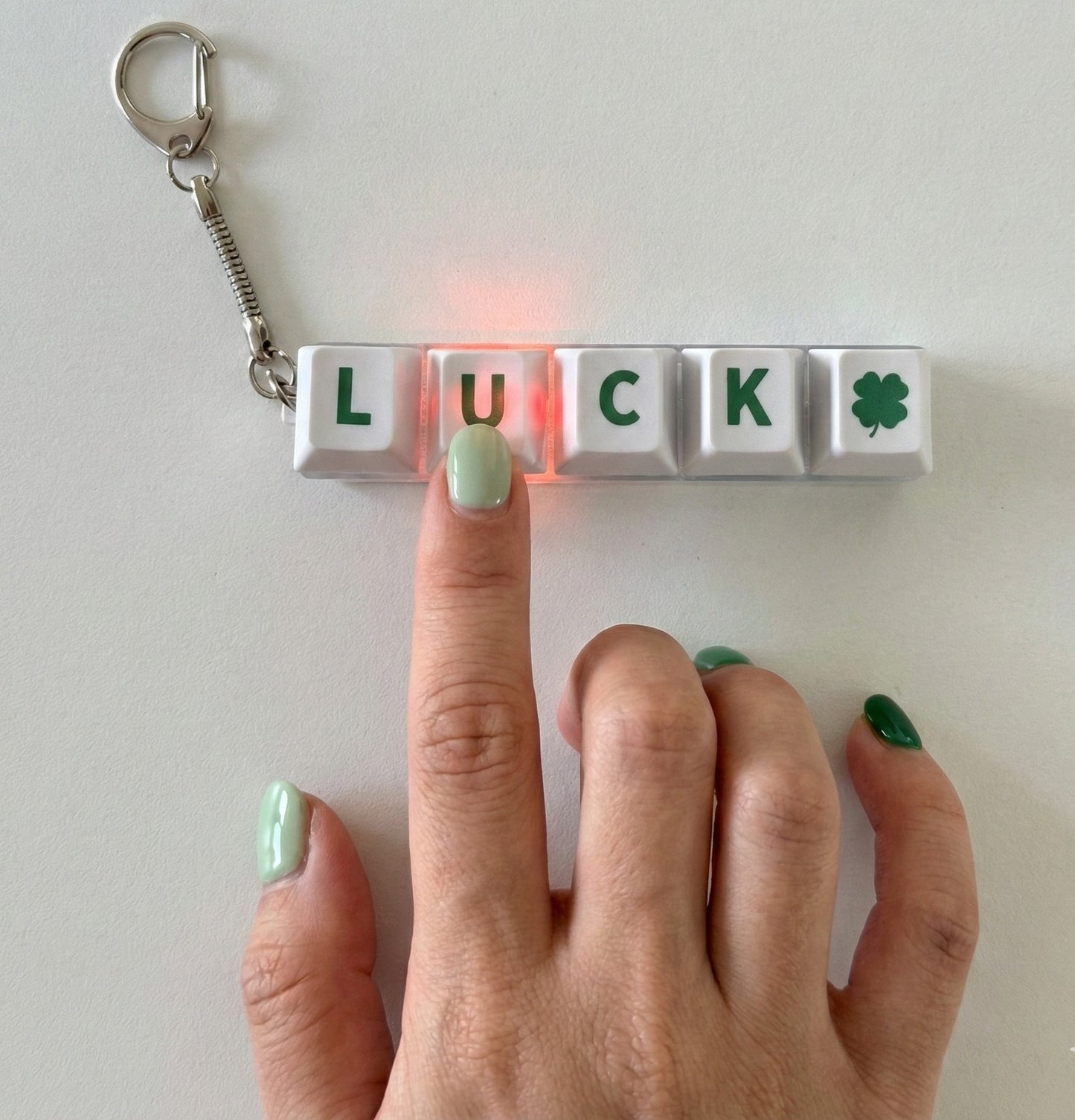 Close-up hand pressing LUCK mechanical keychain with pink LED light illuminating