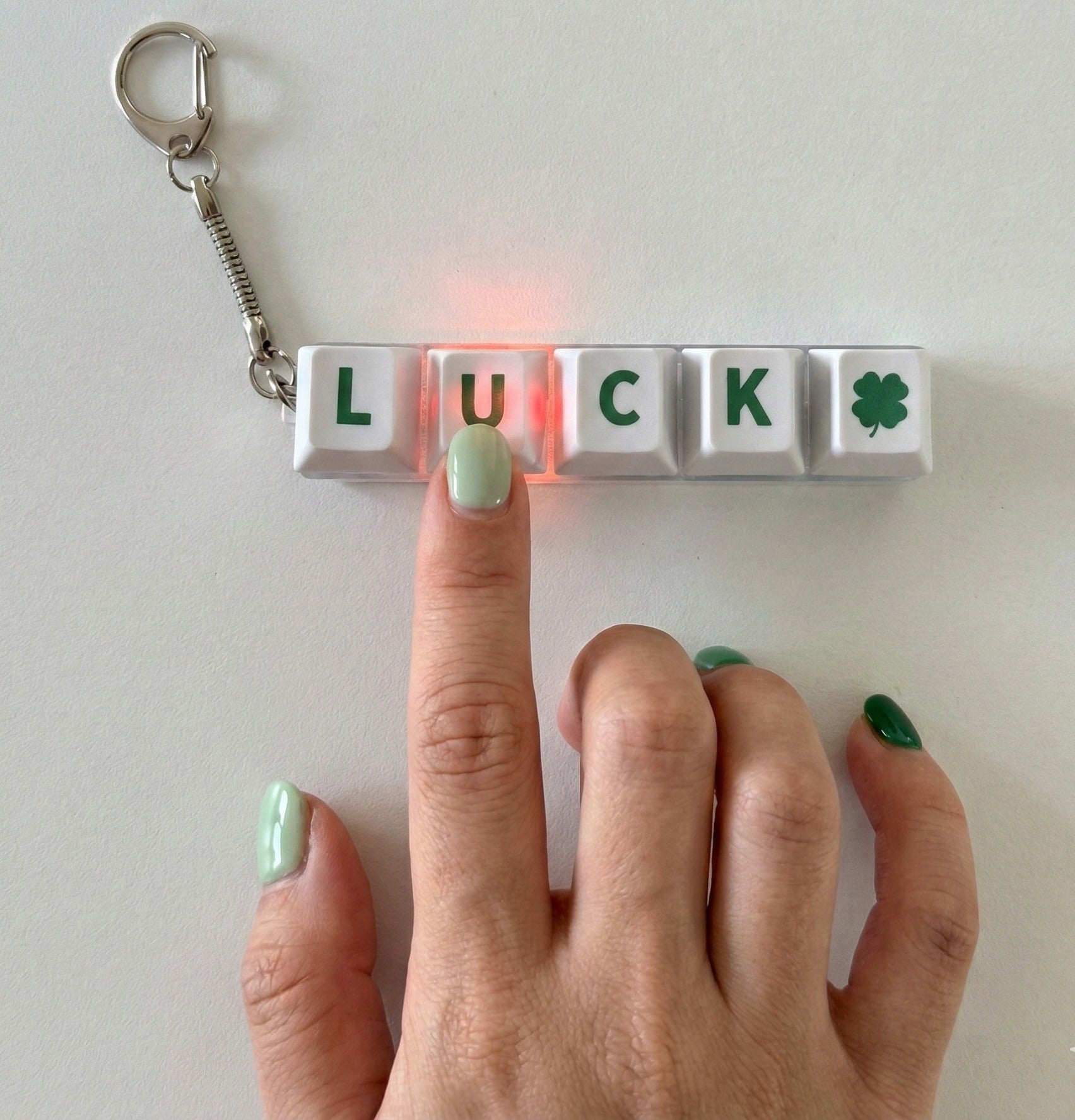 Close-up hand pressing LUCK mechanical keychain with pink LED light illuminating