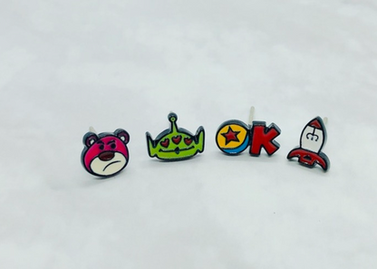 Flat lay of all four Toy Story character earrings - Lotso, Alien, Rocket and Pixar Ball