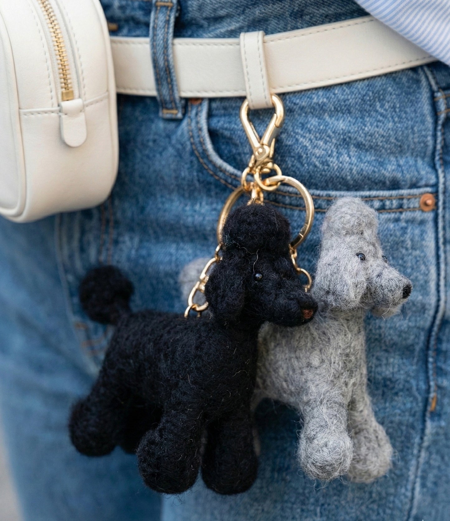  Double poodle keychains in black and grey attached to denim backpack with cream crossbody bag