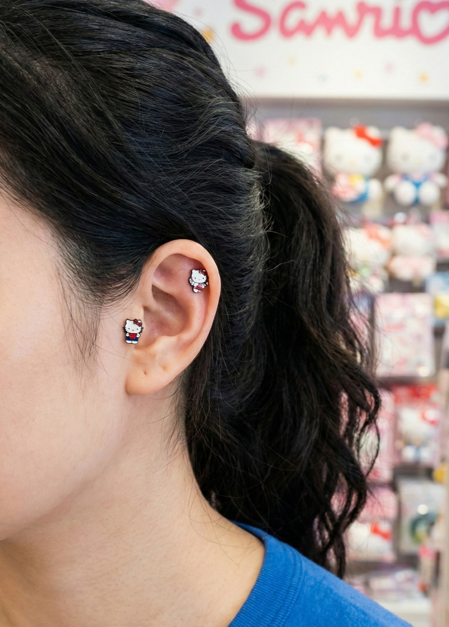 Sanrio Hello Kitty enamel studs worn on ear with Kitty collectibles background, ideal gift for Sanrio fans