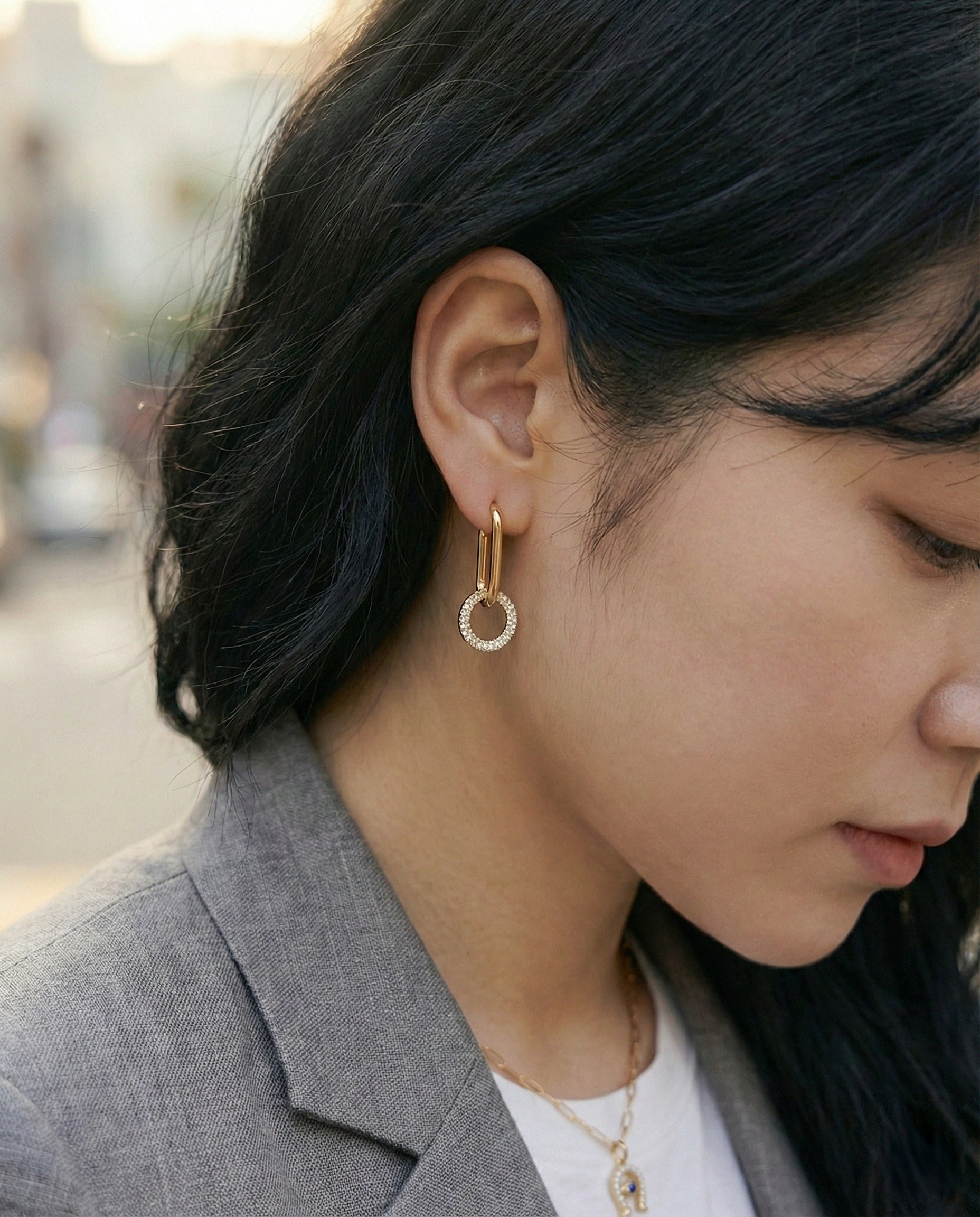 Outdoor shot of woman wearing gold oval link drop earrings, professional style