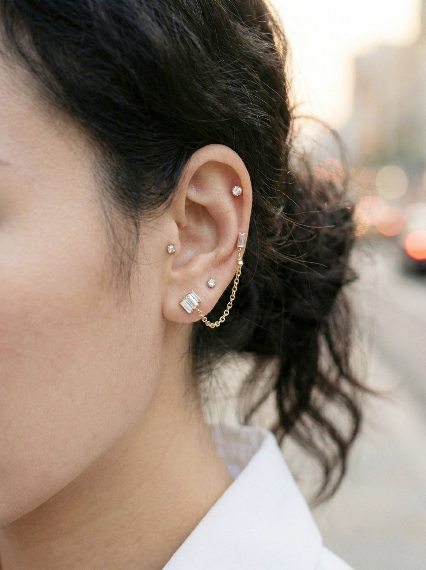 Close-up of layered ear piercings with baguette crystal chain connector