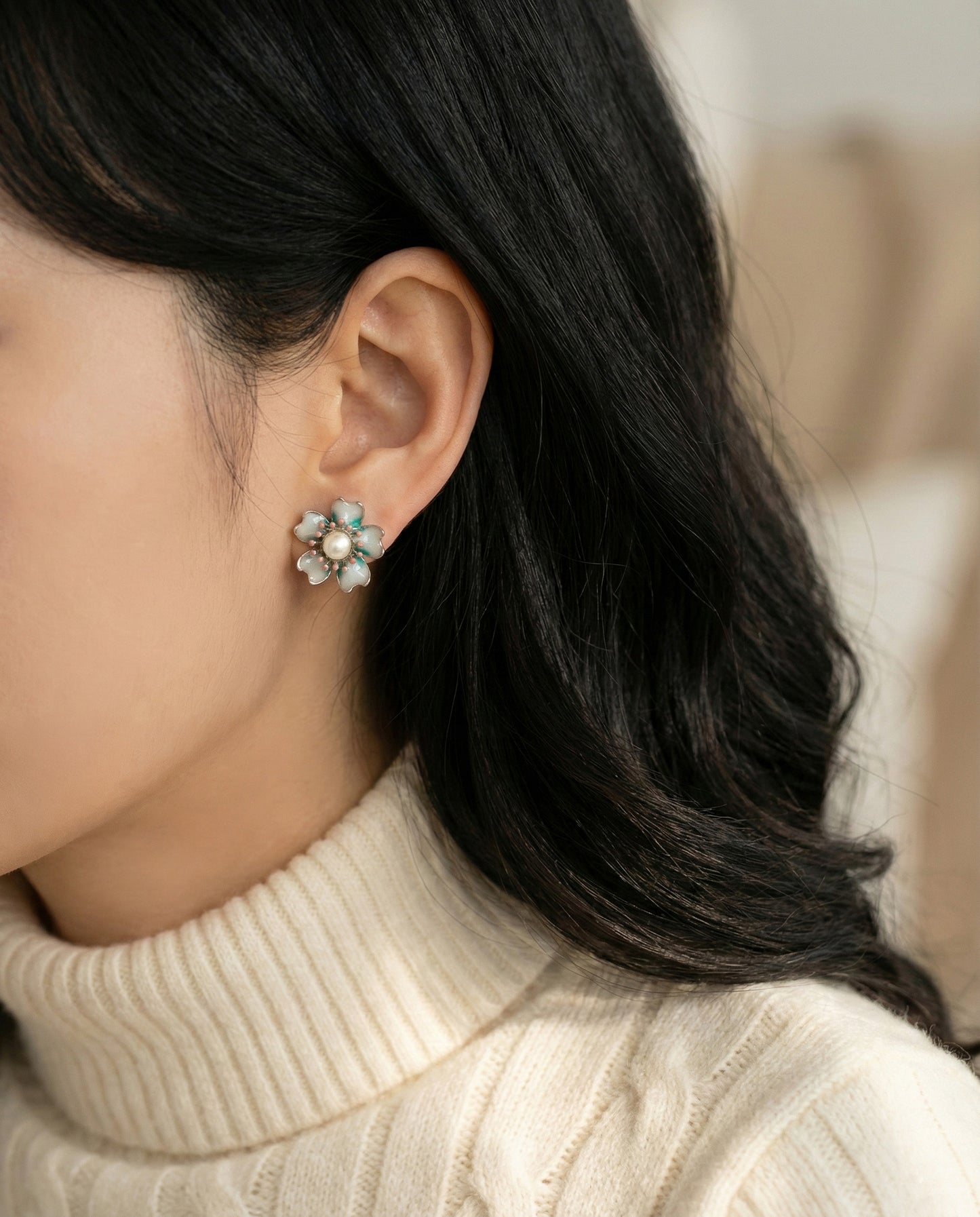 Model wearing iridescent teal-green enamel flower studs with pearl, shown from back angle with dark hair