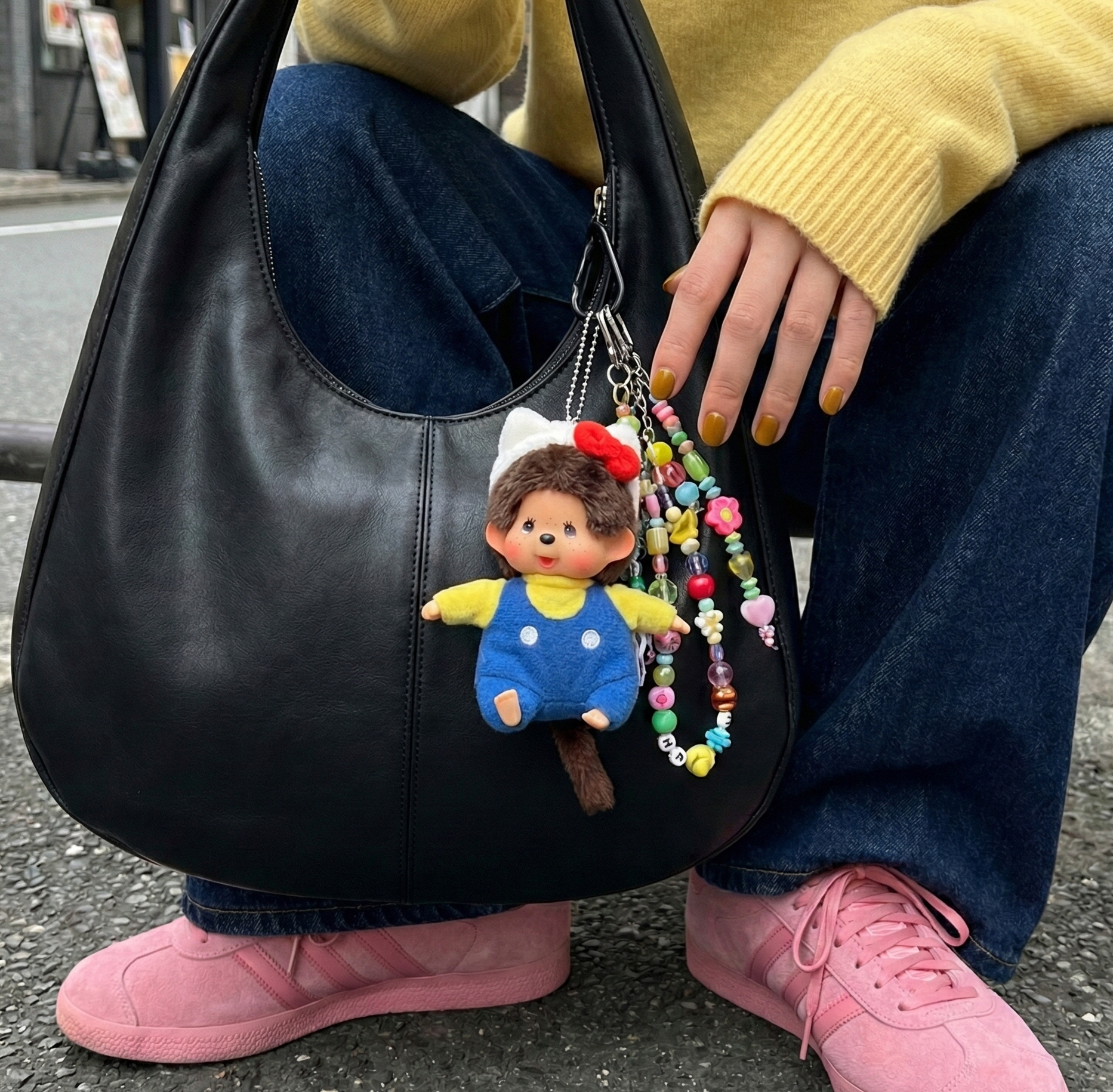 Close-up of Monchhichi keychain on black bag with yellow knit sweater and pink sneakers