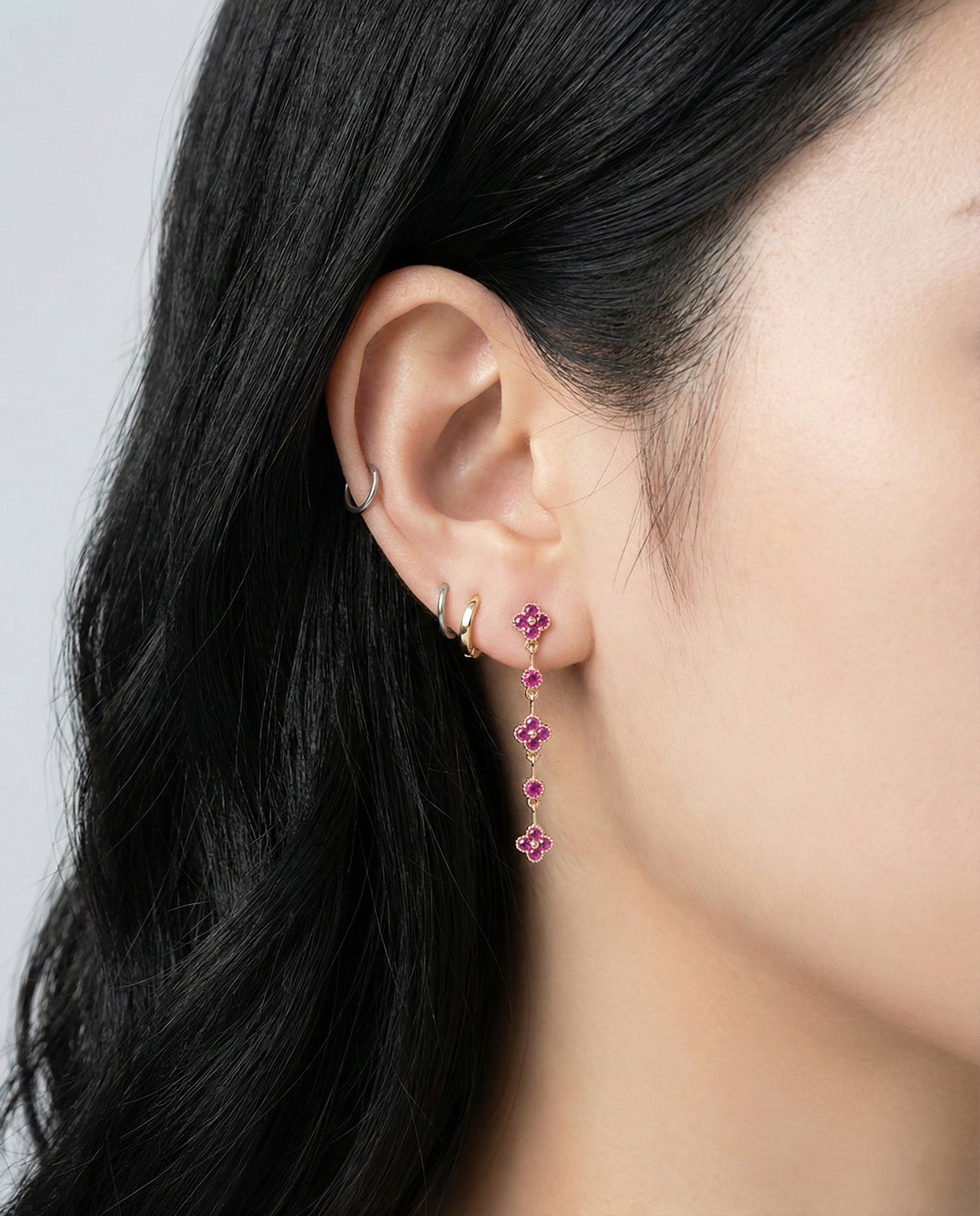 Ruby red clover earrings styled with multiple piercings showing versatile layering