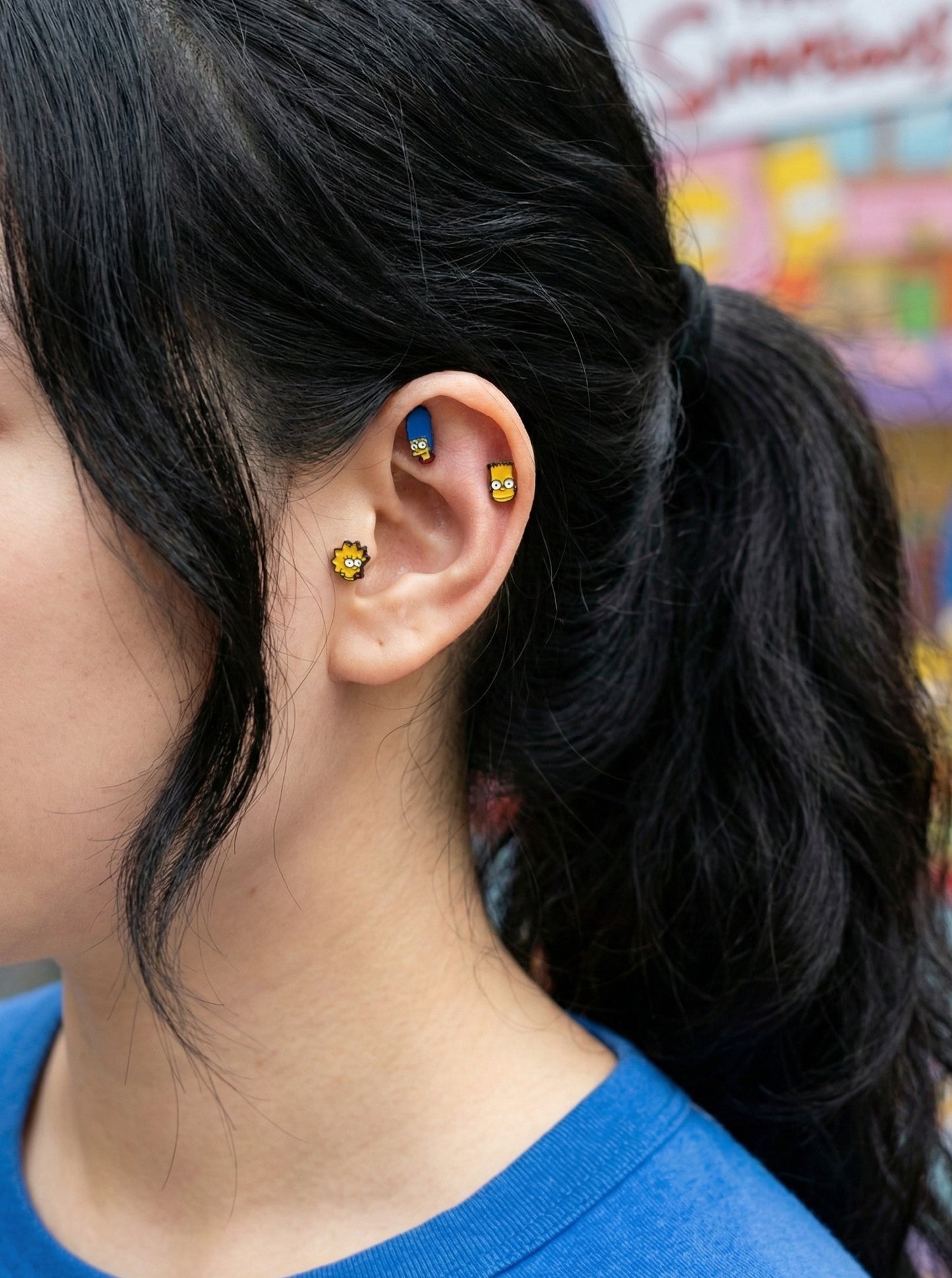 Simpsons character piercings worn on ear - Marge in helix, Bart in conch, Lisa in lobe, layered ear stack styling
