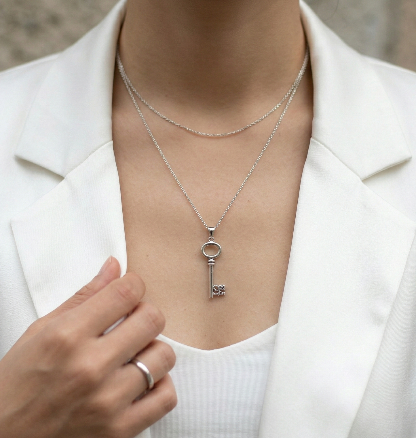 Chic layering of the silver key necklace over a white blazer and tank top, professional yet unique.