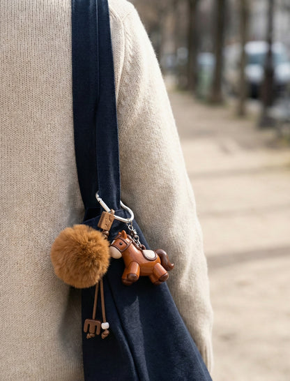 Brown pony bag charm hanging on navy crossbody bag with beige sweater outfit
