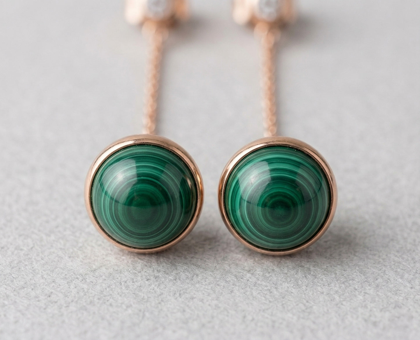 Extreme macro close-up of two 8mm natural malachite cabochon stones in rose gold bezel setting, showing distinctive swirling green banding patterns