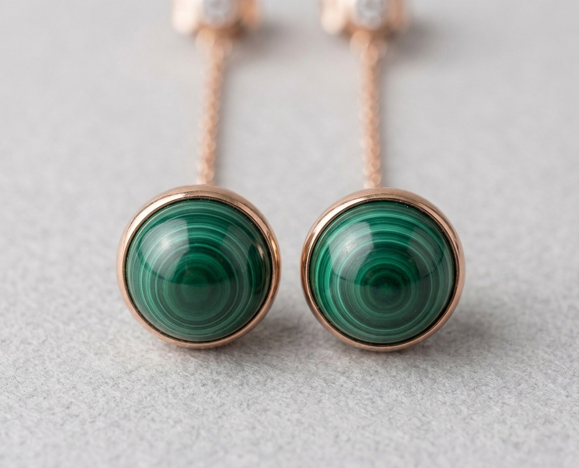 Extreme macro close-up of two 8mm natural malachite cabochon stones in rose gold bezel setting, showing distinctive swirling green banding patterns