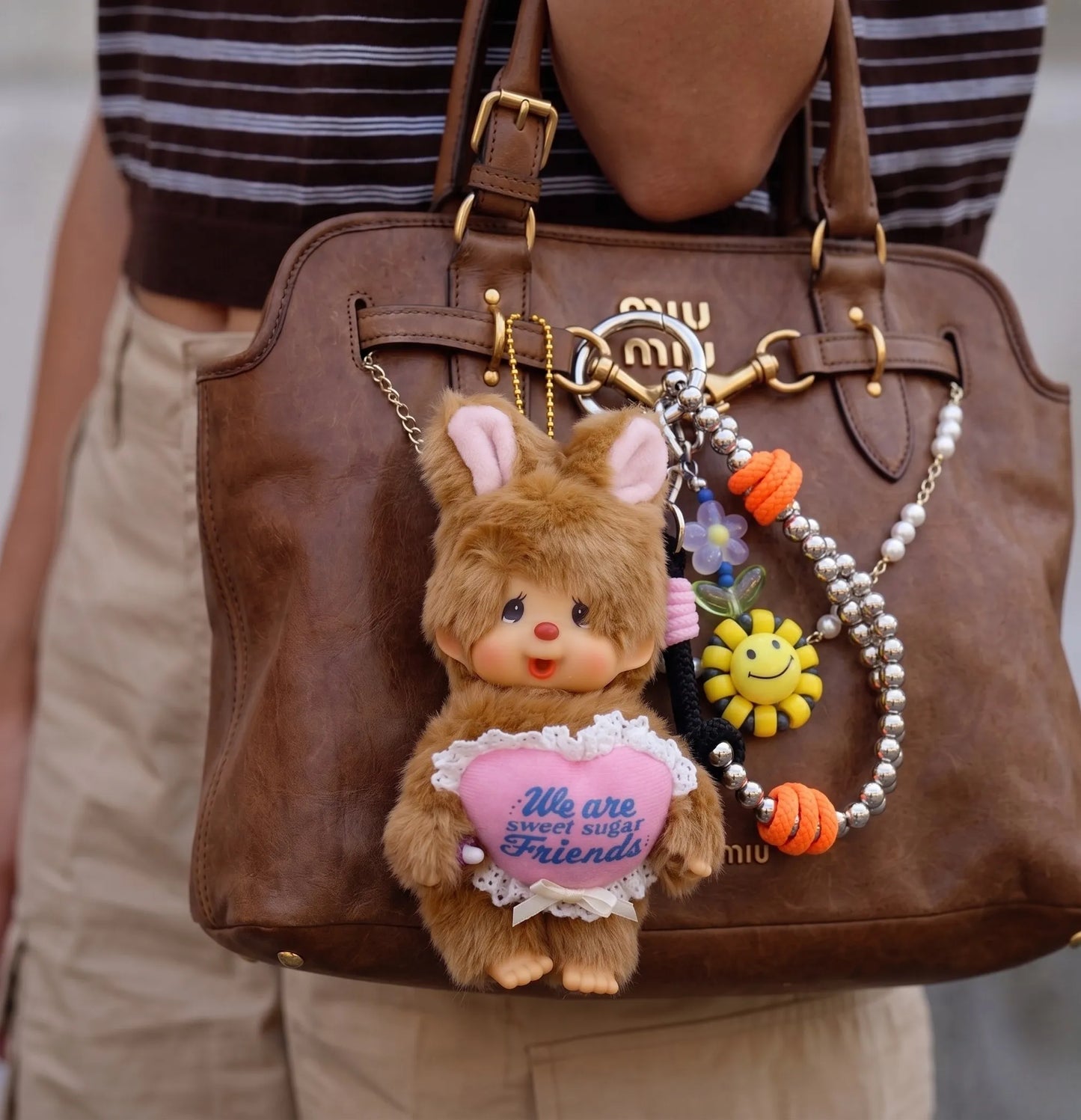 Downtown girl bag charm 8ttitto8 silver smiley flower bead strap keychain with Monchhichi on Miu Miu vintage bag, outdoor candid.
