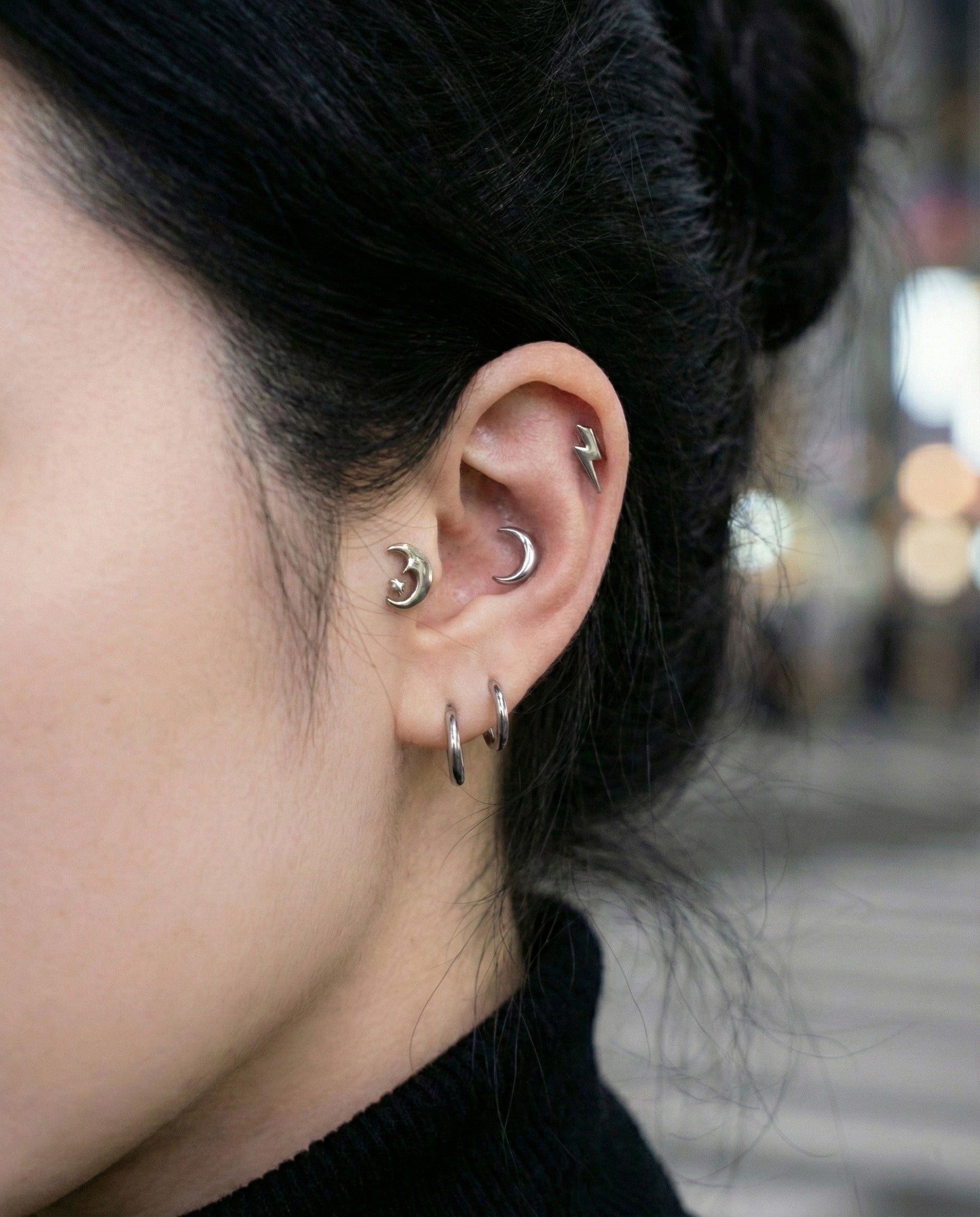 Close-up of crescent moon and lightning bolt surgical steel studs on ear