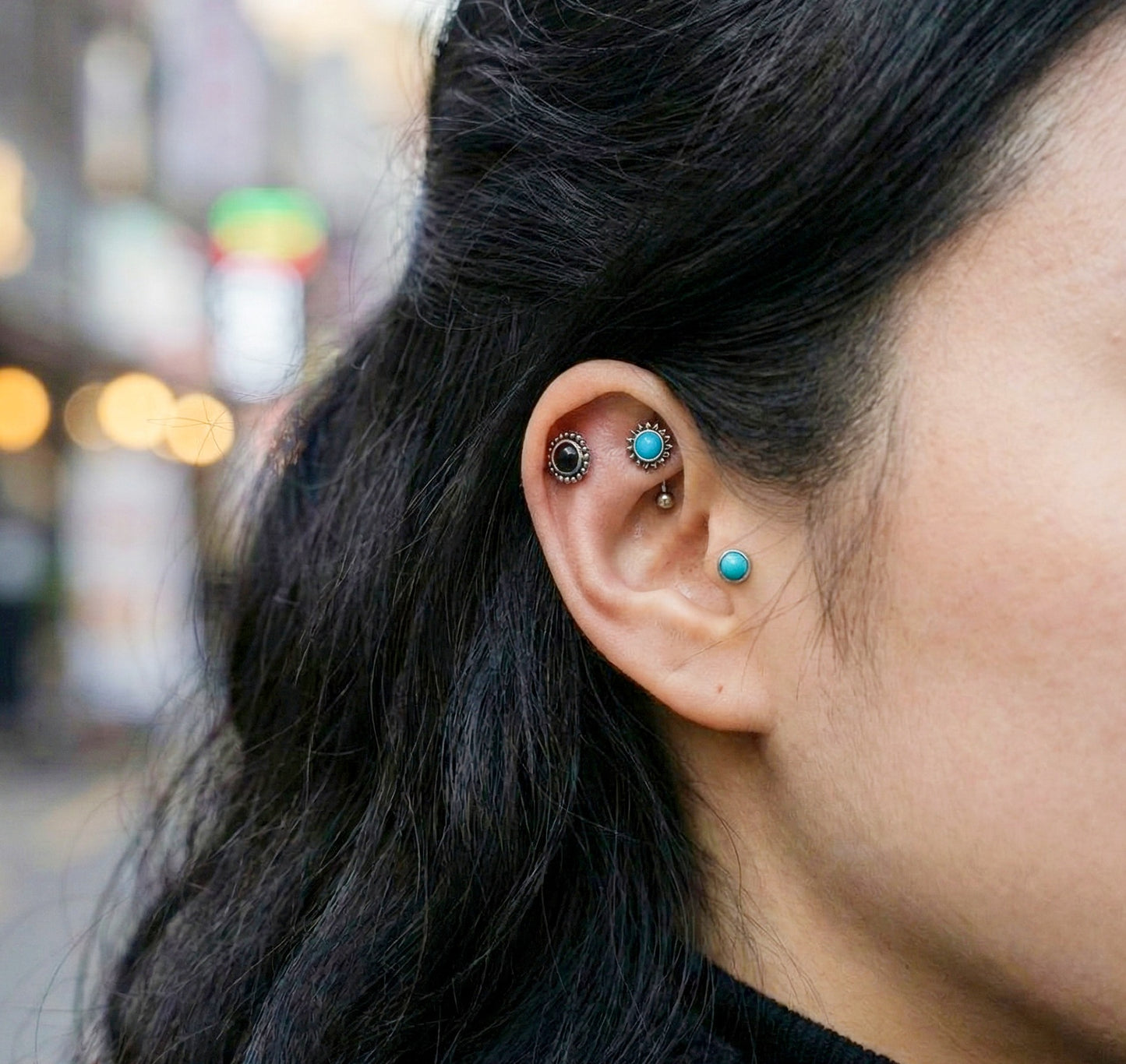 Side view of ear showing layered barbell studs in helix, conch, and lobe placements