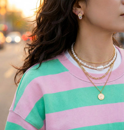 Labubu style earrings styled with pastel striped sweater, pearl necklaces, and gold chain for kawaii fashion look