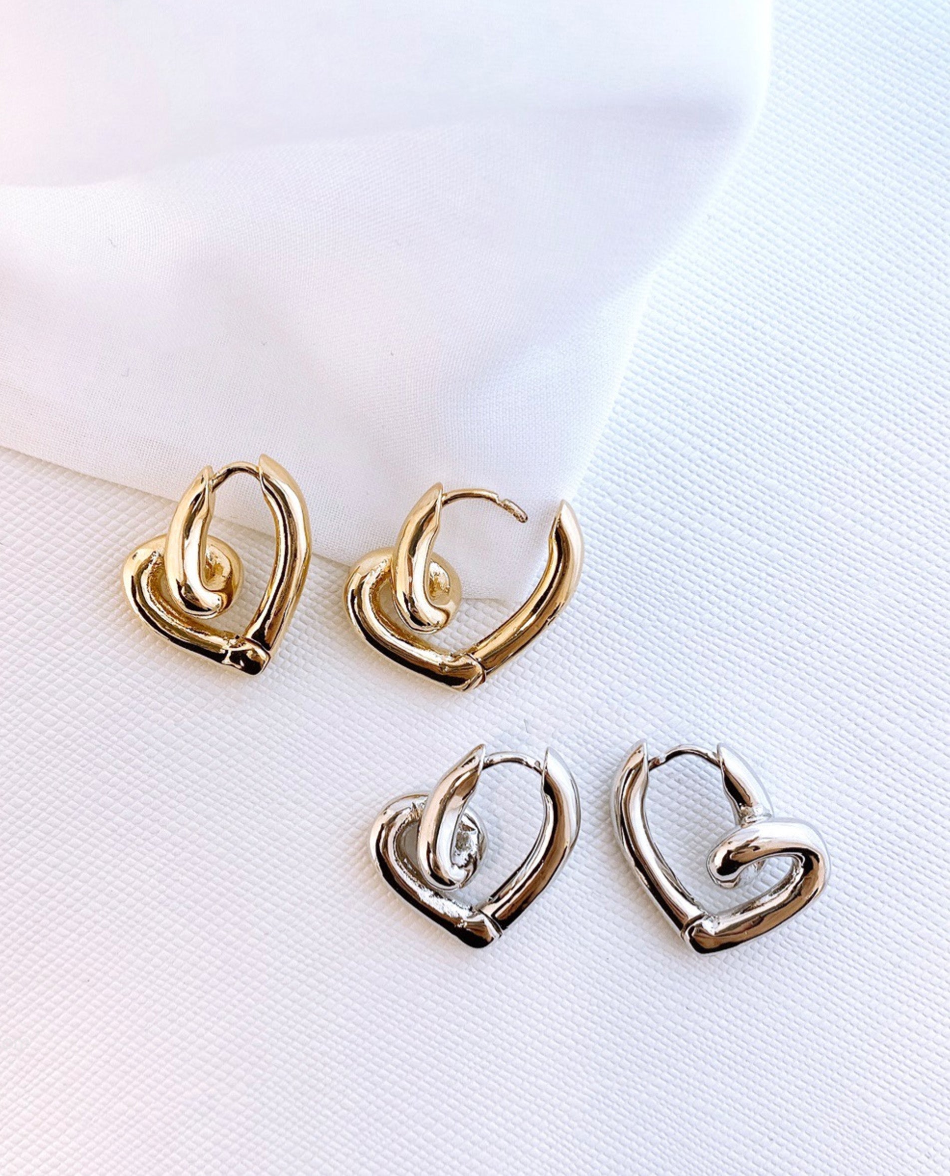 Gold and silver twisted heart hoop earrings side by side comparison on fabric, color options