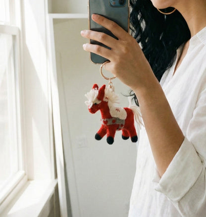 Mirror selfie showing white shirt outfit with red horse keychain hanging from wrist on gold ring, minimalist styling`