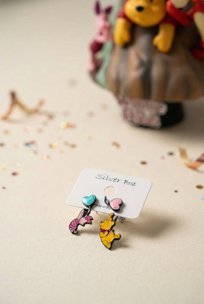 
Winnie the Pooh and Piglet earrings on display card with figurines in background

