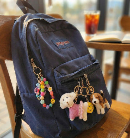 Navy blue backpack styled with multiple keychains including wool felt poodle and smiley face charms