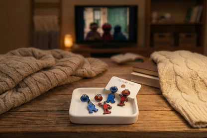 Full Sesame Street earring set displayed on cozy wood tray; Elmo and Cookie Monster in both face and body variants, styled for a holiday gift scene.