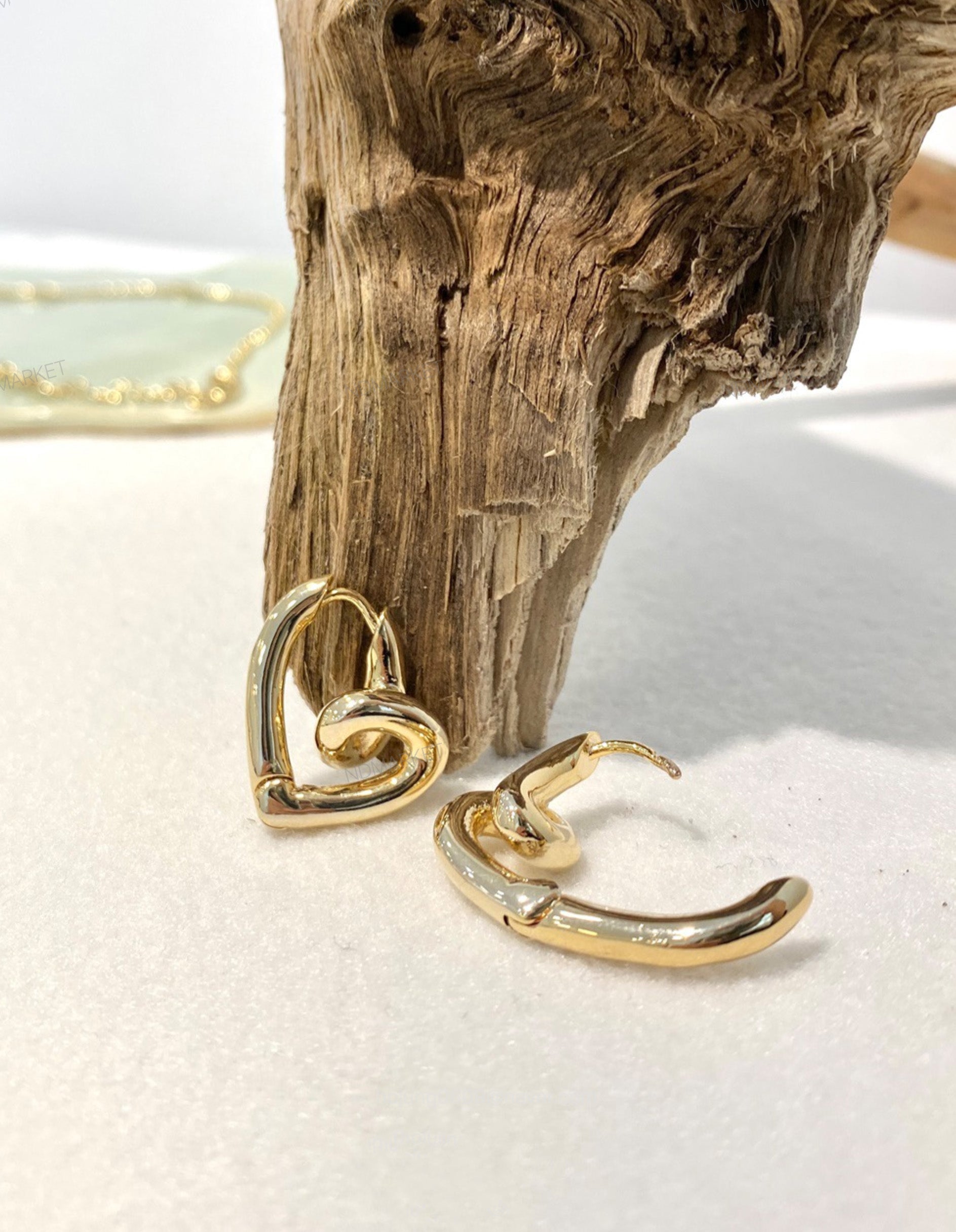 Gold sculptural heart huggie earrings displayed on driftwood with dimensional knot detail visible