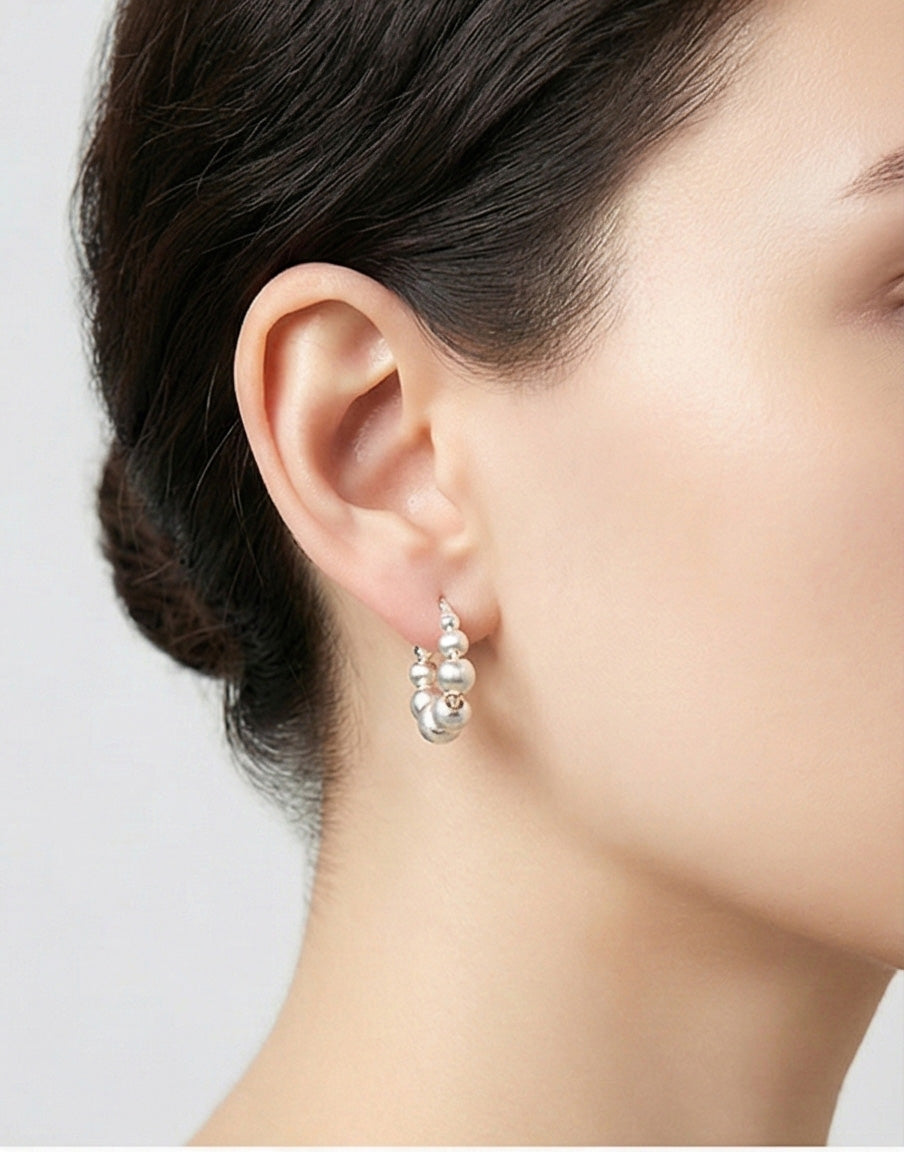 Woman wearing silver textured ball hoop earrings side profile, displaying brushed metal sphere design close to earlobe, lightweight comfortable fit, 925 sterling silver hypoallergenic, minimalist modern style
