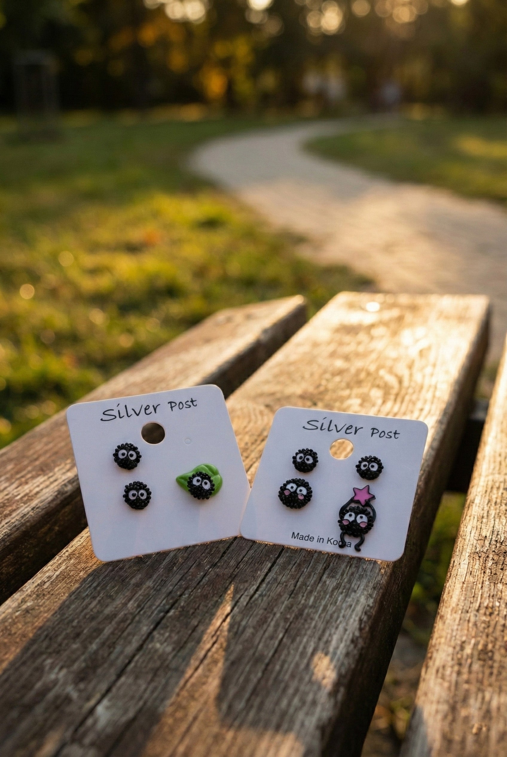 Outdoor photo of both earring card sets on wooden bench in natural lighting showing green and pink accents