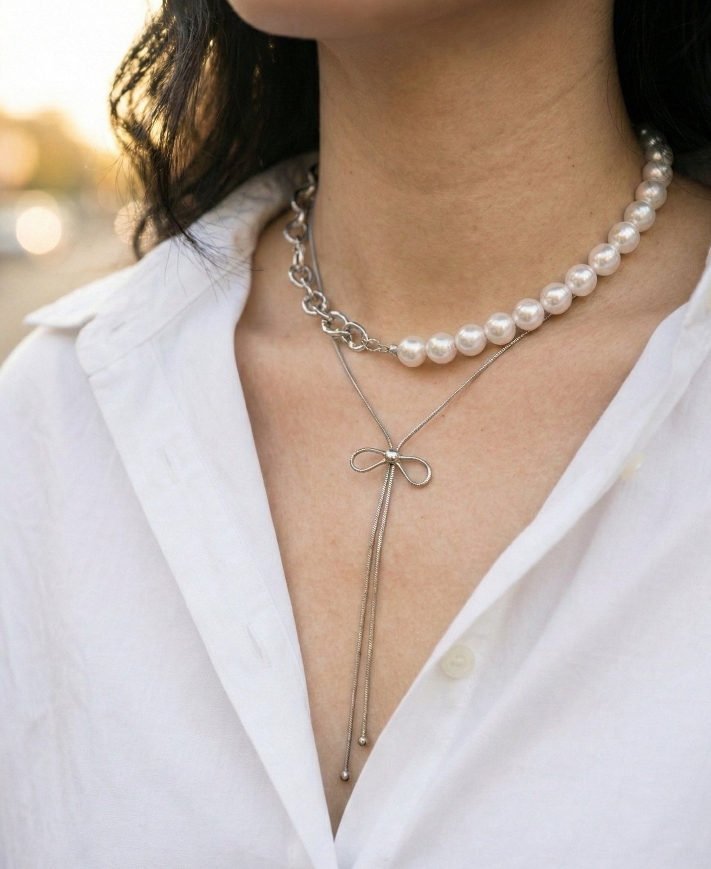 Close-up of gold bow lariat necklace layered with pearl necklace - elegant neck styling