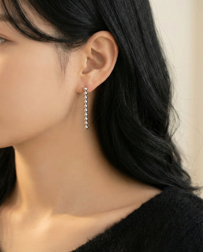 Woman in black top wearing silver ball bar drop earrings - neck and shoulder view