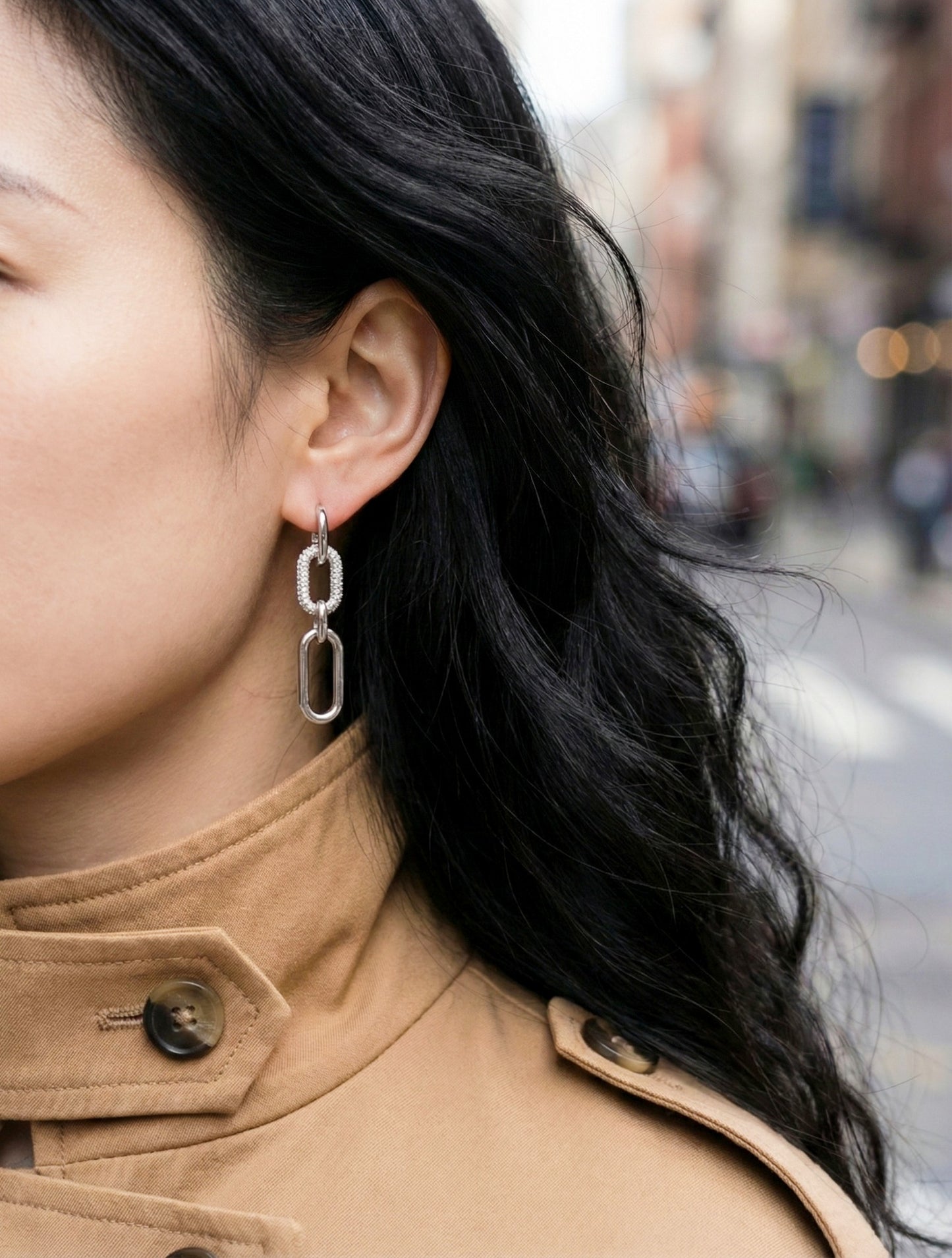 Woman in beige coat wearing silver chain link drop earrings, close-up ear view