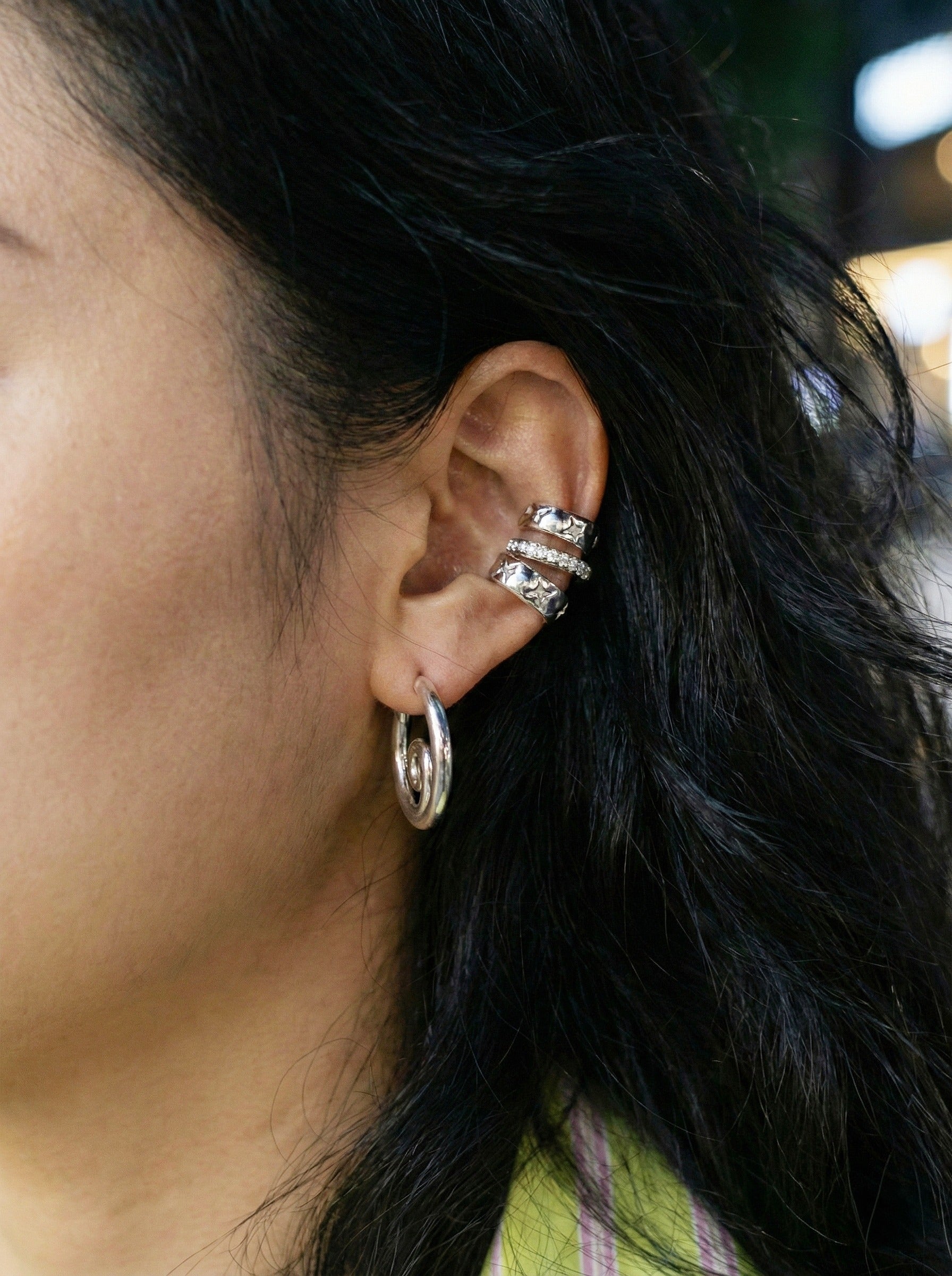 Model wearing silver spiral hoops outdoors with colorful striped shirt and city lights