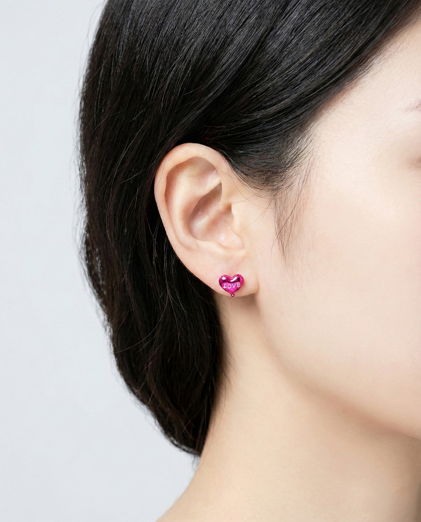 Woman wearing magenta pink heart balloon earring on ear with black hair
