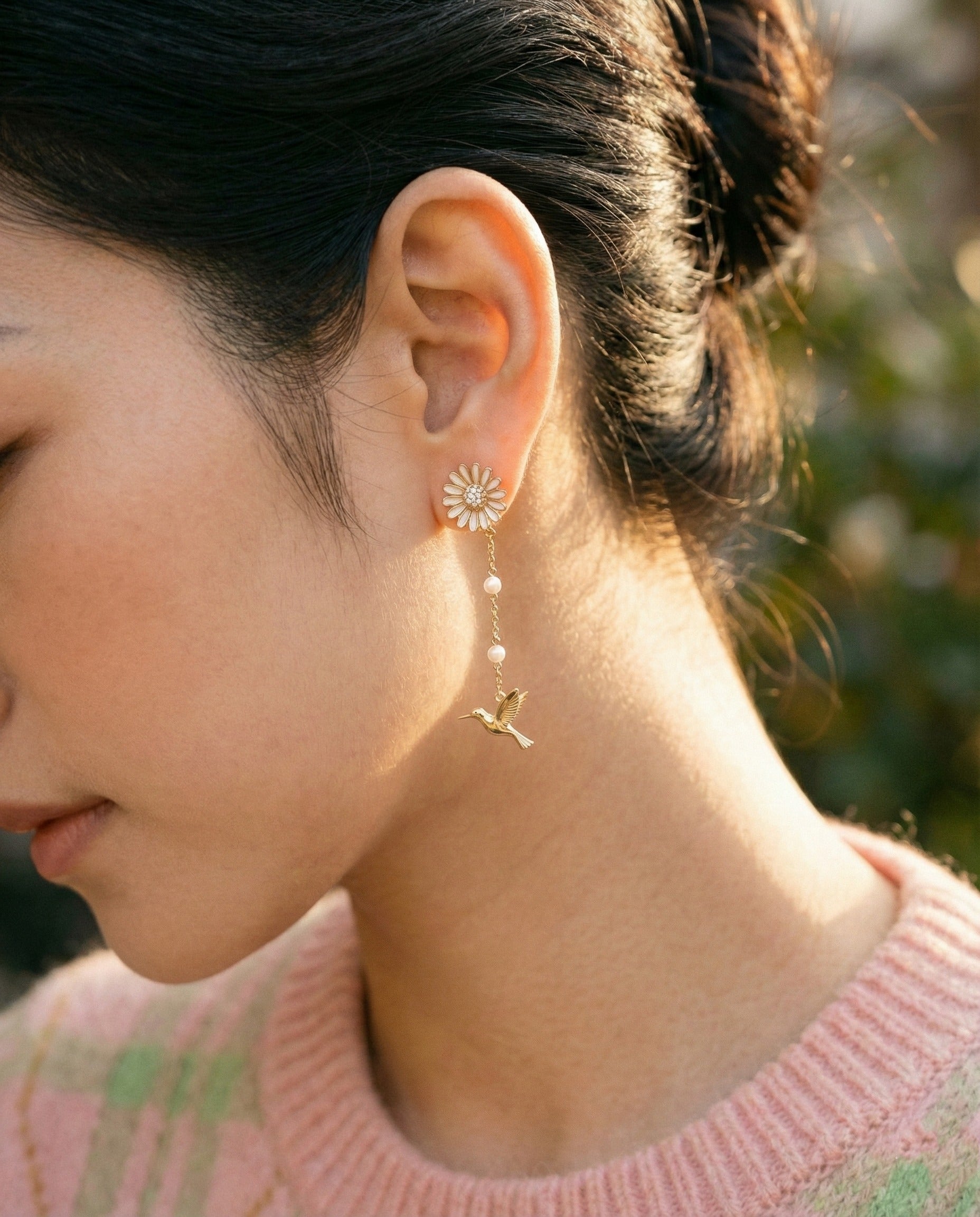 Model in pink sweater wearing silver daisy hummingbird earrings outdoors