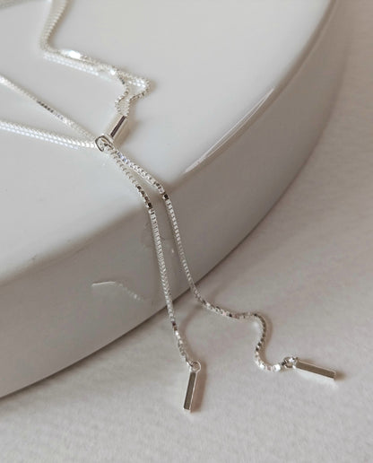 Glossy silver Y-drop necklace resting on ceramic tray, featuring slim vertical pendants