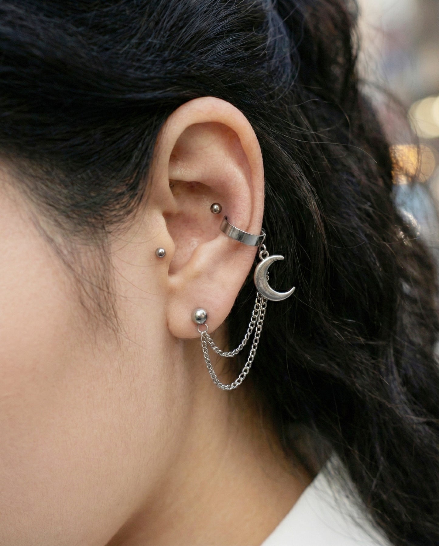 Close-up of an ear with multiple earrings and dark hair.