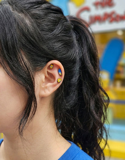 The Simpsons enamel earrings displayed on ear - Homer, Marge, Lisa, and Bart characters arranged vertically