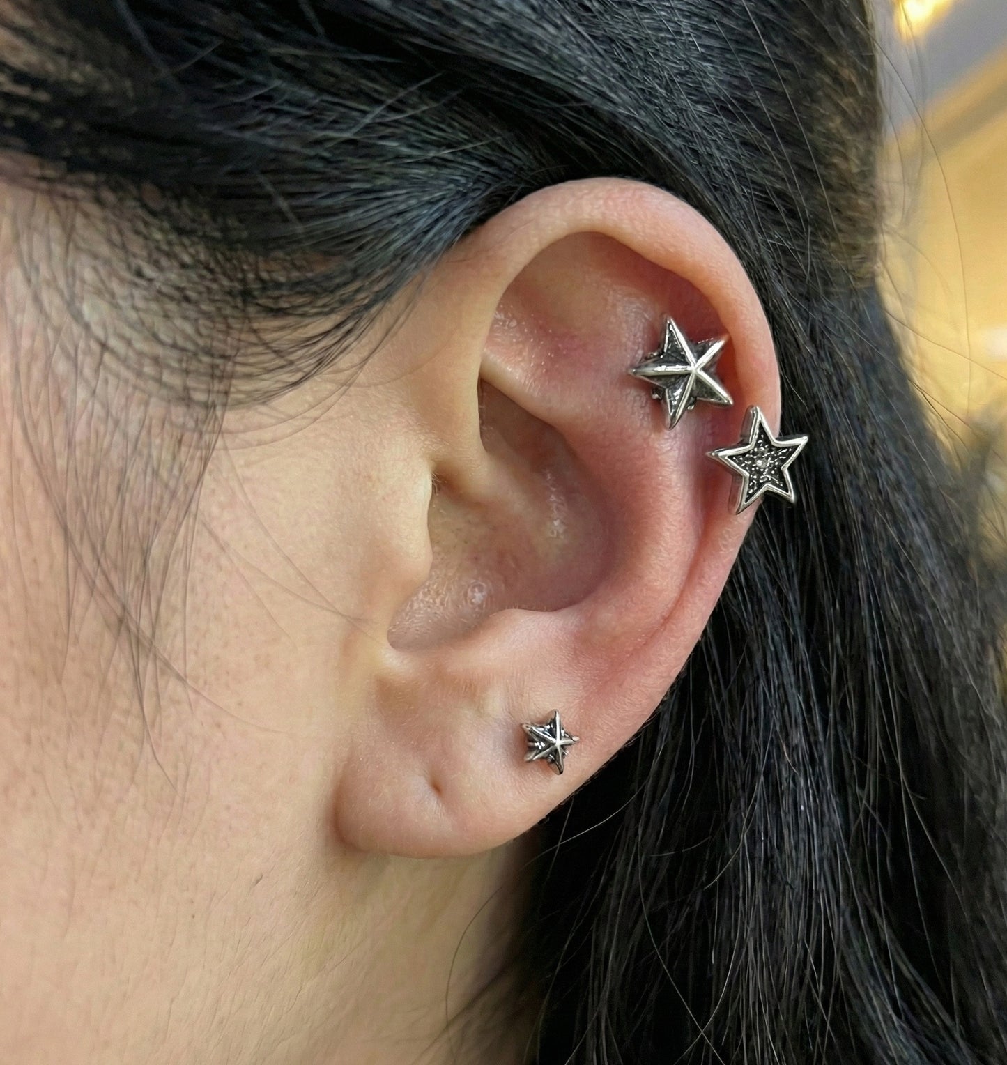 Close-up of model's ear featuring three Y2K chunky star piercings layered from outer conch to lobe