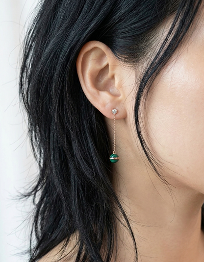 
Model with long dark hair wearing malachite chain drop earrings against white background, rose gold chain visible between hair strands