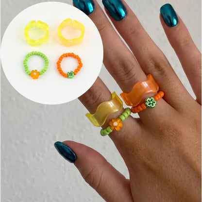 K-fashion stacked ring aesthetic — bold orange wave resin ring and flower beaded ring layered with chrome blue nails, summer vacation jewelry