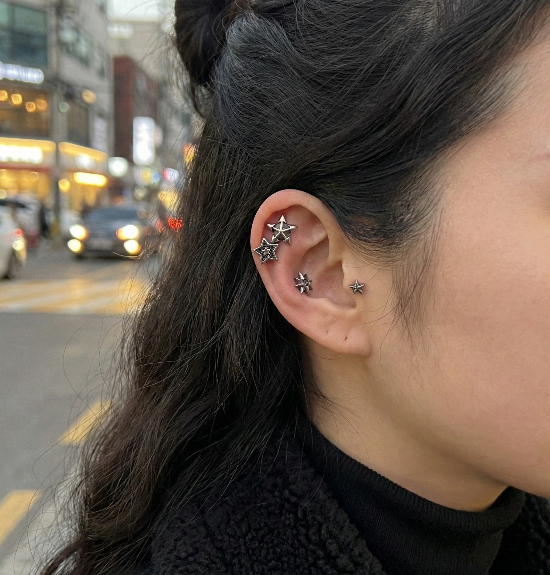 Model wearing vintage star barbell piercings in multiple ear positions against bokeh night street background