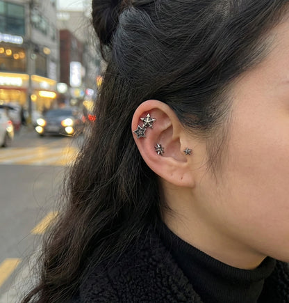 Model wearing vintage star barbell piercings in multiple ear positions against bokeh night street background