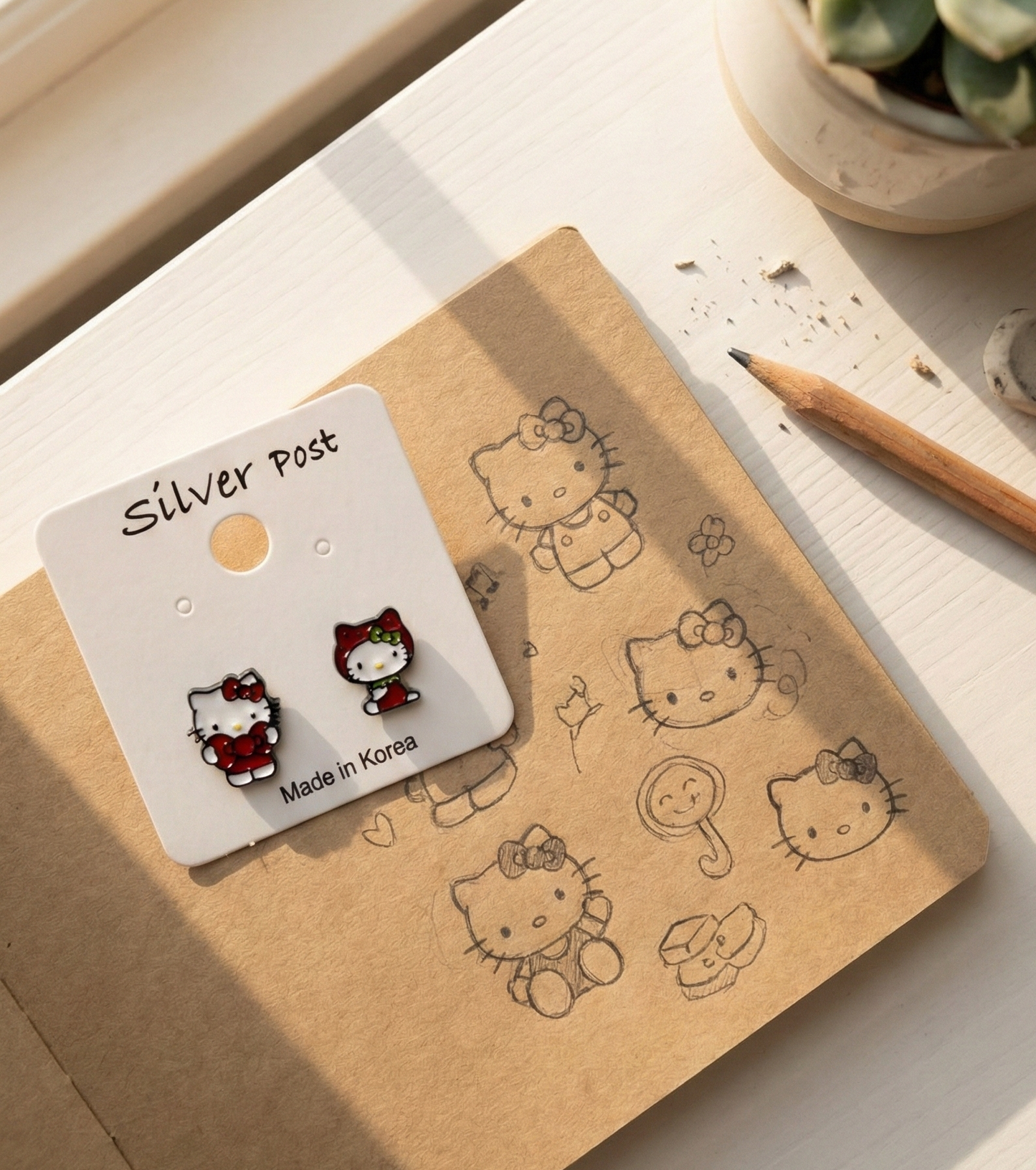Kawaii Hello Kitty stud earrings displayed on craft notebook with hand-drawn Sanrio characters