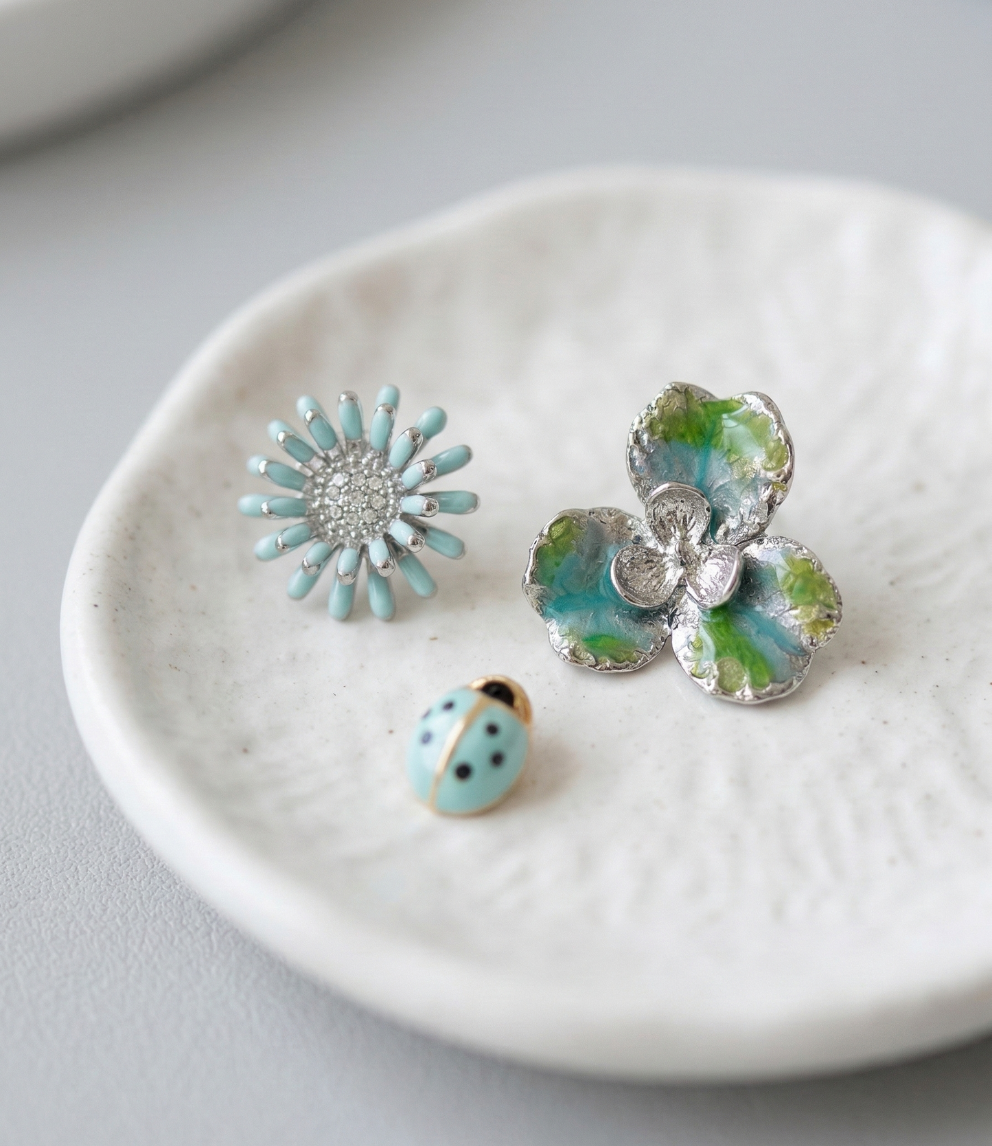 Fresh Mint floral and ladybug 3-piece earring set elegantly displayed on a white textured ceramic small plate.