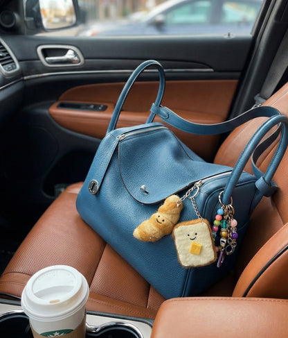 Felt bakery keychains attached to blue leather bag in car interior - toast and croissant charms