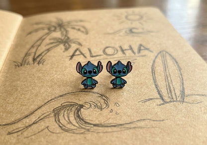 Pair of blue alien ear jacket earrings displayed on wooden board with ALOHA engraving, Hawaiian theme