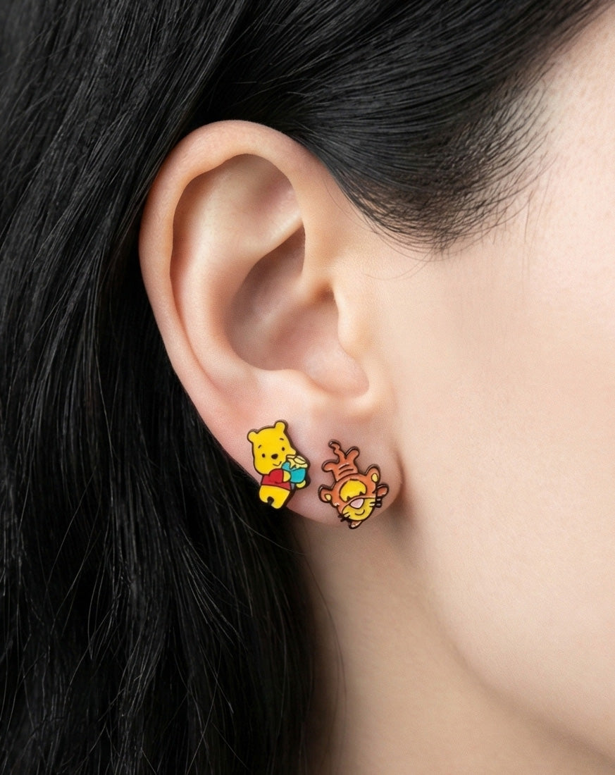 Woman wearing Disney Pooh and Tigger mismatched stud earrings, yellow and orange enamel characters