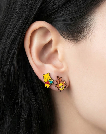 Woman wearing Disney Pooh and Tigger mismatched stud earrings, yellow and orange enamel characters