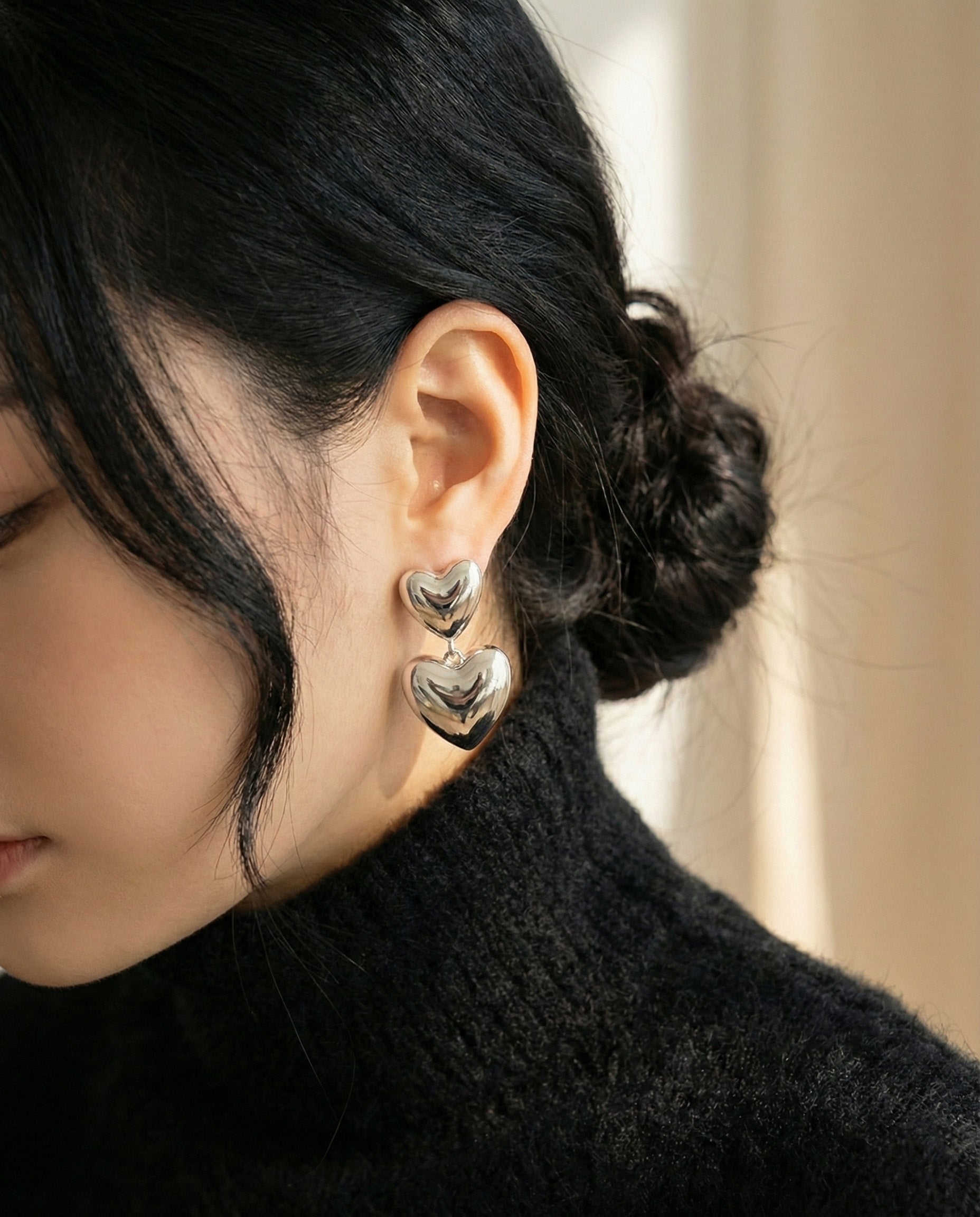 Close-up of silver heart drop earrings worn with black turtleneck - modern minimalist look