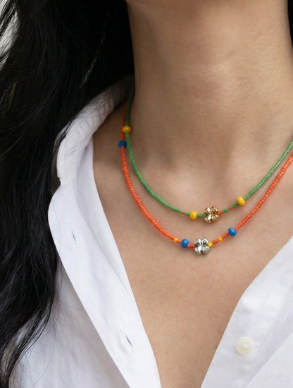 Woman's neck and shoulder showing layered green and orange seed bead choker necklaces with white shirt