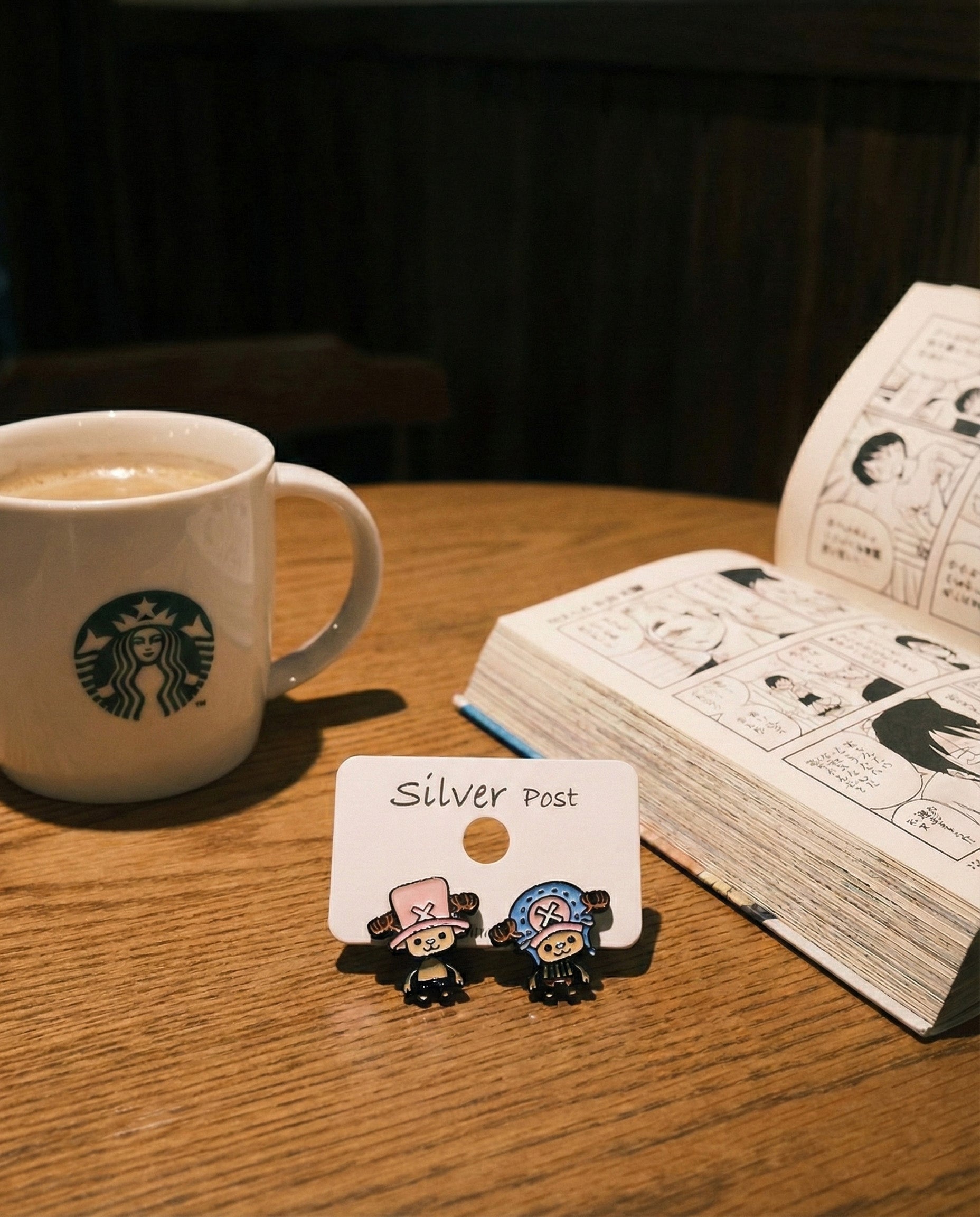 Chopper earring set displayed on wooden cafe table with One Piece manga and coffee mug lifestyle shot